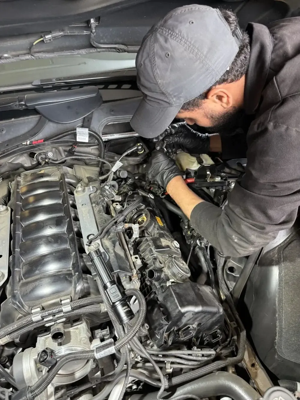 Favio, lead mechanic at Beacon Auto Care San Mateo, working on a 2006 BMW 550i N62 V8 engine bay during a valve cover replacement