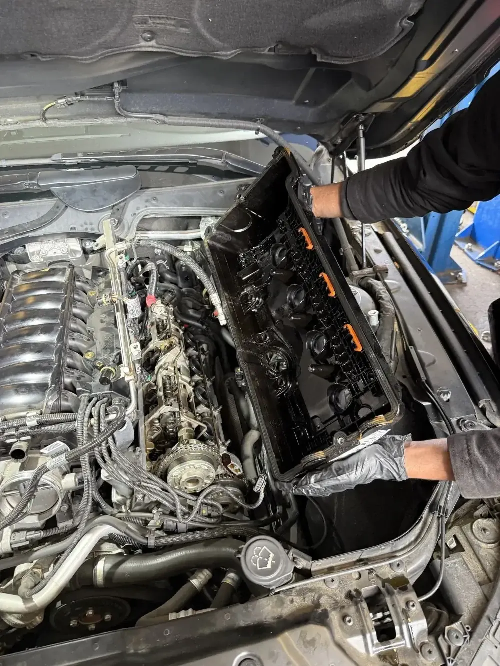 Favio holding the warped OEM BMW N62 plastic valve cover after removal at Beacon Auto Care San Mateo